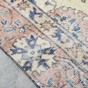 May include: Close-up of a vintage rug with a cream background and a repeating pattern of blue and pink floral designs.