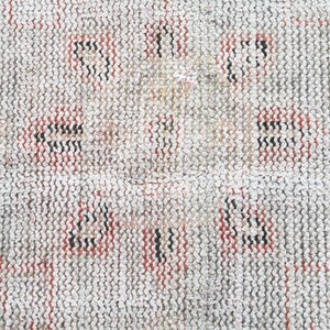 May include: Close-up of a white woven rug with a repeating pattern of red and black lines.