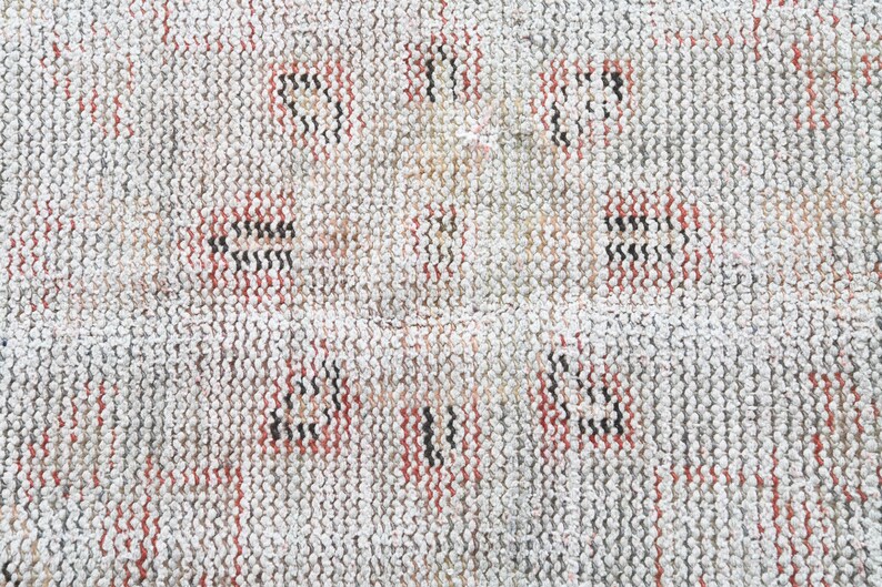 May include: Close-up of a white woven rug with a repeating pattern of red and black lines.