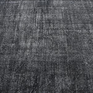 May include: A close-up of a dark gray textured rug with a subtle pattern. The rug has a distressed look, giving it a vintage feel.