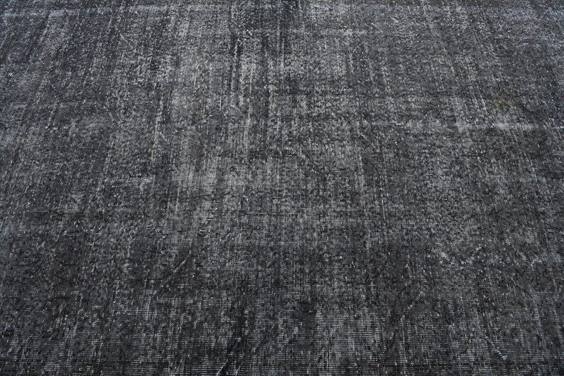 May include: A close-up of a dark gray textured rug with a subtle pattern. The rug has a distressed look, giving it a vintage feel.