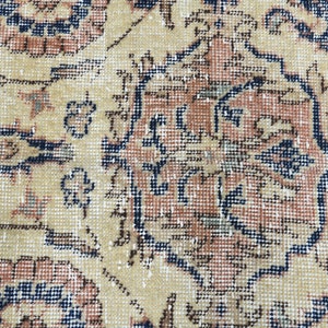May include: Close-up of a beige rug with a detailed floral pattern in shades of blue, red, and brown. The rug has a worn, vintage look.