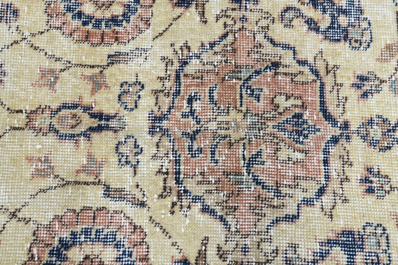 May include: Close-up of a beige rug with a detailed floral pattern in shades of blue, red, and brown. The rug has a worn, vintage look.