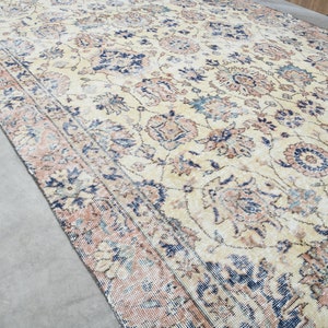 May include: A vintage rug with a cream background and a floral pattern in shades of blue, pink, and brown. The rug has a distressed look, with faded colors and a worn texture.