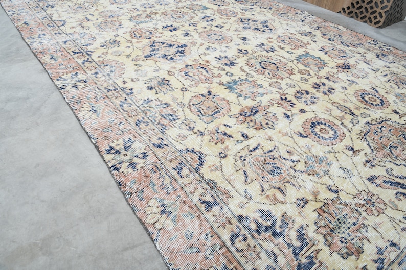 May include: A vintage rug with a cream background and a floral pattern in shades of blue, pink, and brown. The rug has a distressed look, with faded colors and a worn texture.
