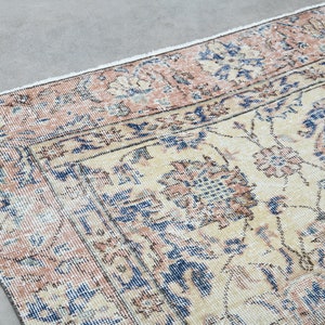 May include: A vintage rug with a cream background and a floral pattern in shades of pink, blue, and brown. The rug has a distressed look, with faded colors and a worn texture.