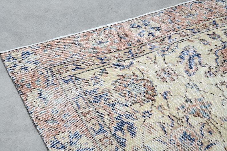 May include: A vintage rug with a cream background and a floral pattern in shades of pink, blue, and brown. The rug has a distressed look, with faded colors and a worn texture.
