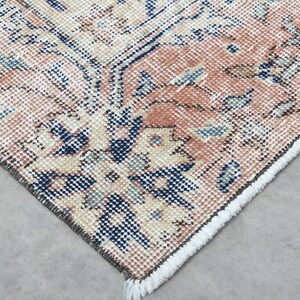 May include: Close-up of the edge of a rug with a floral pattern in shades of pink, blue, and cream. The rug has a fringe border.
