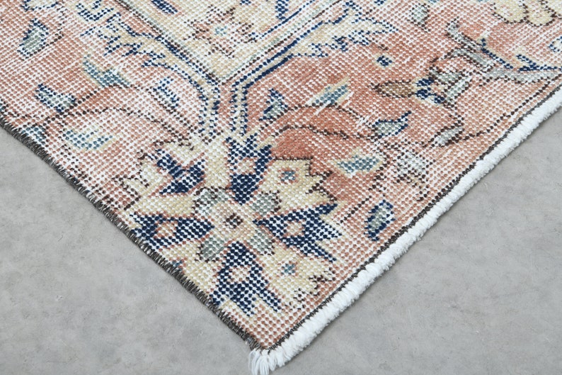 May include: Close-up of the edge of a rug with a floral pattern in shades of pink, blue, and cream. The rug has a fringe border.