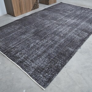 May include: A dark gray rug with a distressed, vintage look. The rug has a subtle pattern and a white border.
