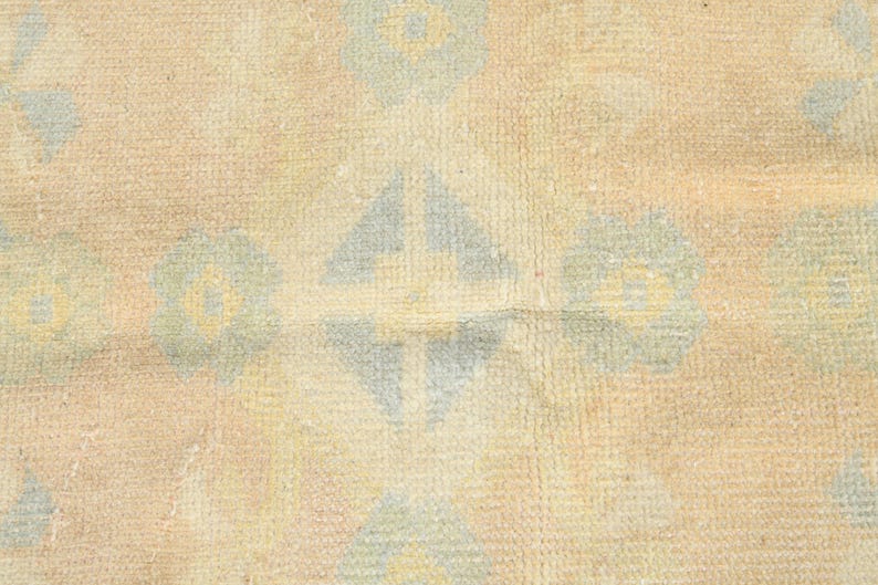 Op de afbeelding: Een geweven textielkleed met een herhalend patroon van lichtblauwe en gele bloemmotieven op een getextureerde beige achtergrond. Het ontwerp bevat geometrische ruitvormen afgewisseld met gestileerde bloemelementen over het oppervlak.