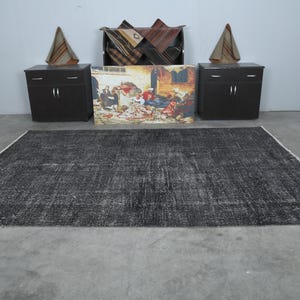 May include: A black and white distressed area rug with a subtle pattern. The rug is laid out on a gray concrete floor.