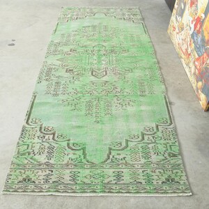 May include: A rectangular runner rug featuring a vibrant mint green base color with intricate, symmetrical geometric patterns in dark brown. The design includes a central medallion and detailed border motifs, creating a balanced visual composition.