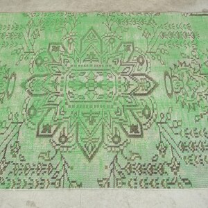 May include: A rectangular area rug featuring a vibrant light green background with a central dark brown geometric floral medallion. The design includes symmetrical botanical patterns and intricate line work extending across the entire surface.