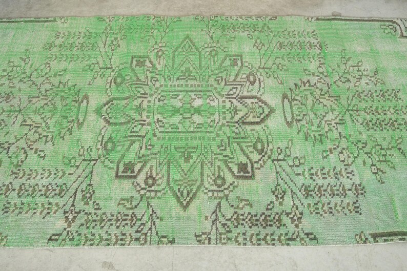 May include: A rectangular area rug featuring a vibrant light green background with a central dark brown geometric floral medallion. The design includes symmetrical botanical patterns and intricate line work extending across the entire surface.