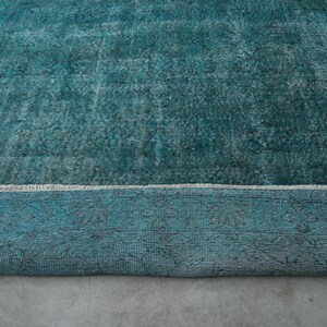 May include: A teal blue rug with a distressed, vintage look. The rug has a white border and a subtle pattern throughout.