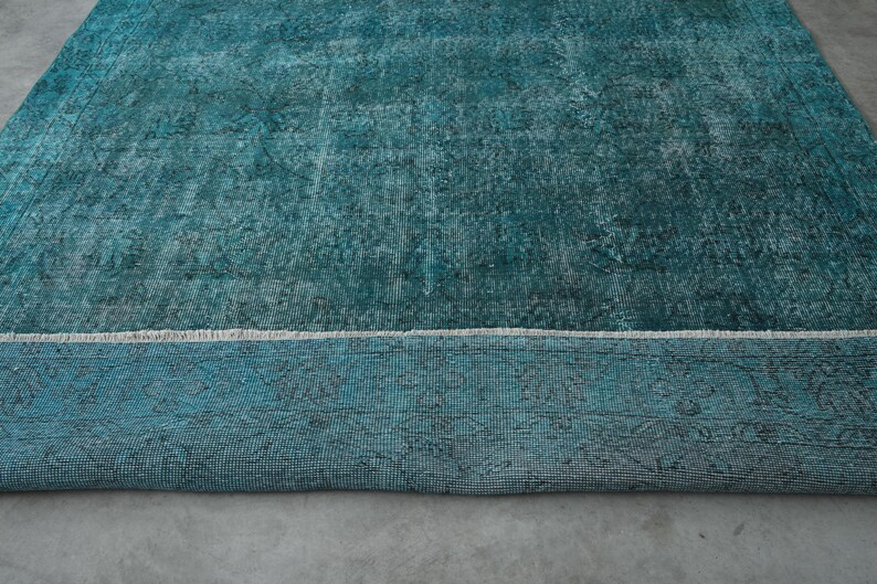 May include: A teal blue rug with a distressed, vintage look. The rug has a white border and a subtle pattern throughout.