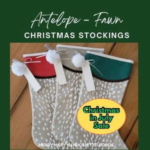 May include: Three Christmas stockings with a fawn pattern and colorful tops. The stockings have red, gray, and green tops with white pom-poms and tags. The image includes the text "Christmas Stockings" and "Christmas in July Sale".