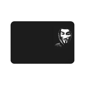 May include: Black rectangular mouse mat featuring the Guy Fawkes mask in grayscale on the right. The mask, a symbol of anonymity, is set against a solid black background.