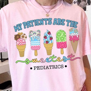 May include: Pink t-shirt with the text "MY PATIENTS ARE THE SWEETEST • PEDIATRICS" and a colorful ice cream graphic. The shirt also has the words "COMFORT COLORS Blossom" in a circular design.