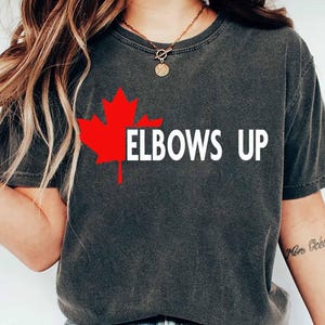 May include: A gray t-shirt with a red Canadian maple leaf and the text "ELBOWS UP" in white.