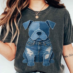 May include: Dark gray t-shirt featuring a denim dog graphic. The dog is made of blue denim patches and wears denim jeans with distressed details. The shirt has a vintage, worn look.