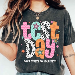 May include: A dark gray t-shirt with a colorful graphic that says "test day" with stars and a "Don't stress! Do your best!" message.