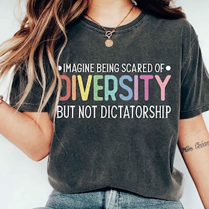 May include: Dark gray t-shirt with the text "IMAGINE BEING SCARED OF DIVERSITY BUT NOT DICTATORSHIP" in colorful letters. The shirt is a crew neck style.
