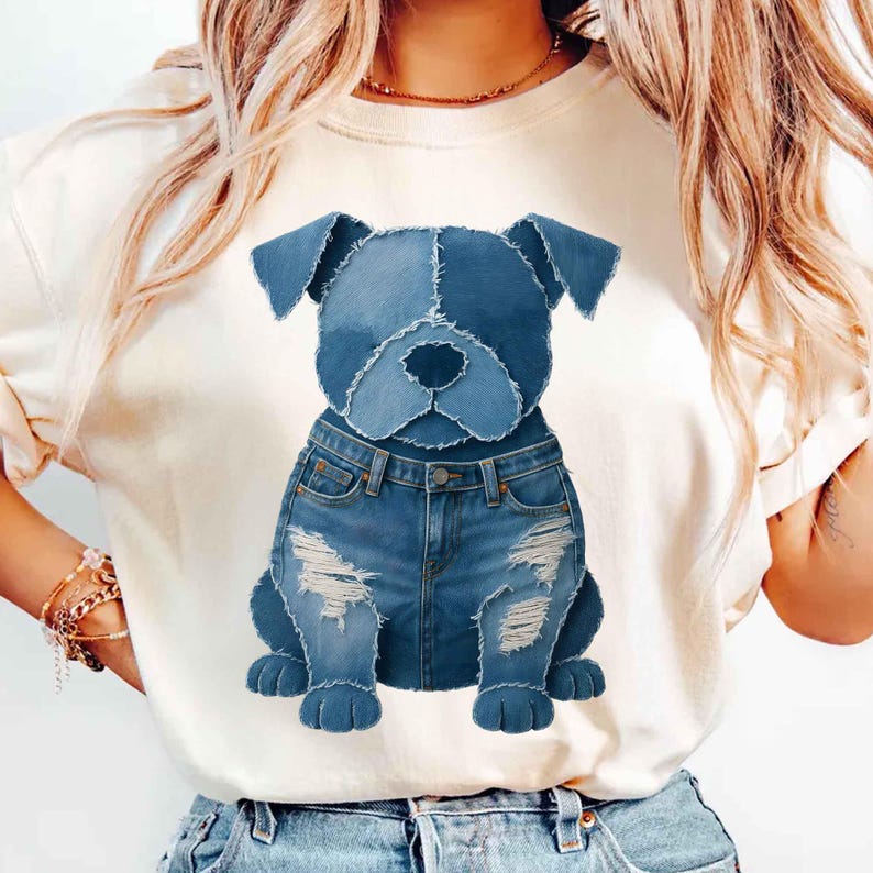 May include: A cream-colored t-shirt featuring a stylized dog design. The dog's head and body are crafted from denim patches in varying shades of blue. The dog is wearing distressed denim jeans, creating a unique and playful aesthetic.