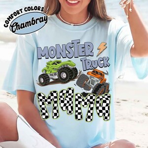 Puede incluir: Camiseta azul claro con la frase "MONSTER TRUCK MAMA" en una fuente divertida. El dise&ntilde;o presenta dos monster trucks, uno verde y otro naranja, con neum&aacute;ticos grandes. La camiseta tambi&eacute;n tiene el texto "COMFORT COLORS Chambray" en un c&iacute;rculo.