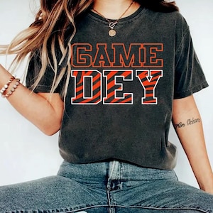 May include: A black t-shirt with the text "GAME DAY" in white letters with an orange and black zebra stripe pattern.