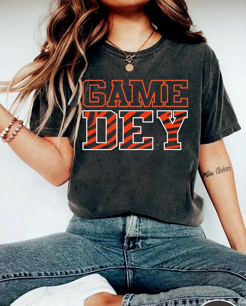 May include: A black t-shirt with the text "GAME DAY" in white letters with an orange and black zebra stripe pattern.