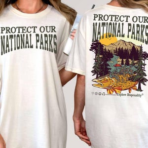 May include: White t-shirt with the text "Protect Our National Parks" printed on the front and a graphic of a fish, mountains, and trees with the text "Protect Our National Parks" and "Explore Responsibly" printed on the back.