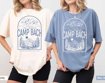 May include: Two oversized t-shirts with a graphic design of a mountain range, a tent, and trees. The text on the shirts reads "JUNE 2025 Ara's Bachelorette CAMP BACH BRECKENRIDGE, CO."