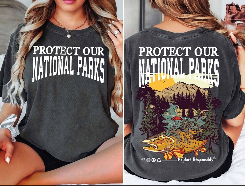 May include: A dark gray t-shirt with the text "Protect Our National Parks" on the front and a graphic of a mountain scene with a fish on the back. The back also includes the text "Explore Responsibly".