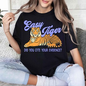 May include: Black t-shirt with a tiger graphic and the text "Easy Tiger" in purple script. Below the tiger is the text "DID YOU CITE YOUR EVIDENCE?" The tiger is orange and black.