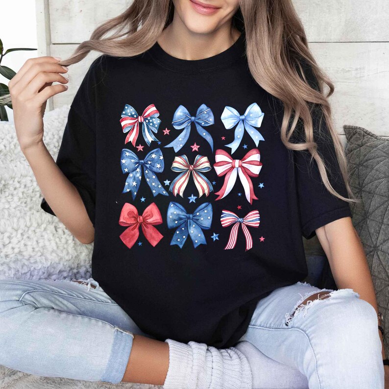 May include: Black t-shirt with a colorful pattern of red, white, and blue bows. The bows are arranged in a grid pattern and have a watercolor effect.
