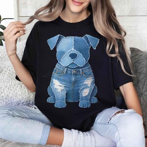 May include: Black t-shirt featuring a denim dog graphic. The dog is depicted wearing denim shorts with distressed details. The graphic is centered on the shirt, creating a playful and casual look. The shirt is made of a soft material.