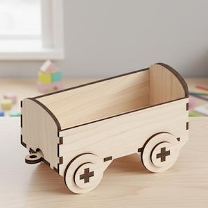 May include: A light brown wooden toy wagon. The wagon features a rectangular body with rounded edges and two wheels on each side, each with a cross design. The toy wagon is designed for toy storage.