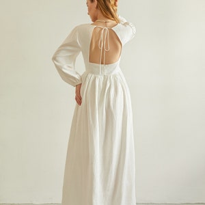 May include: A white maxi dress with long sleeves and a low back with a tie detail. The dress is made of a lightweight fabric and has a flowing silhouette.