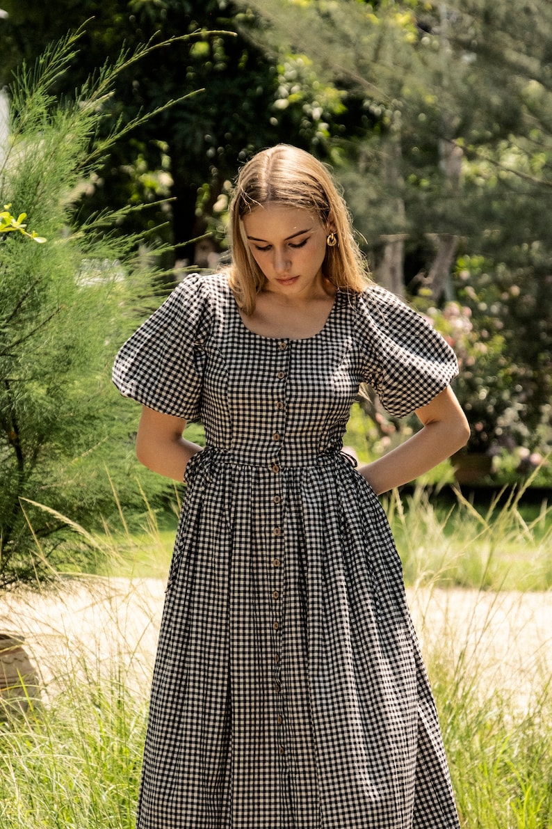 Puede incluir: Una mujer lleva un vestido de cuadros negros y blancos con mangas abullonadas y cierre de botones. El vestido tiene un corpi&ntilde;o ajustado y una falda fluida.
