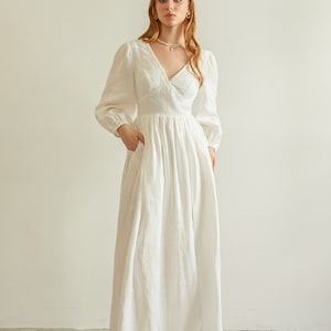 May include: A white linen maxi dress with a V-neckline, long sleeves, and a gathered skirt. The dress has a relaxed fit and a flowy silhouette.