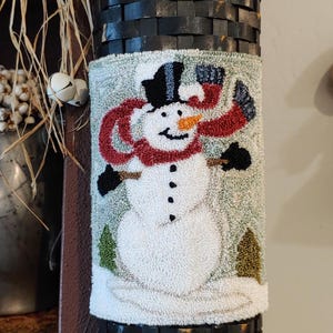 May include: A black woven basket with a decorative snowman applique. The snowman has a black top hat, a red scarf, and black mittens. The basket is cylindrical and appears to be made of wood.