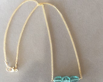 May include: A gold chain necklace with three teal blue glass beads.