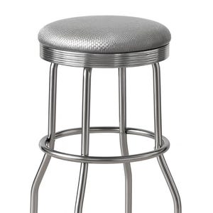 May include: A silver-colored, retro-style bar stool. It features a round, padded seat with a textured pattern and a chrome-finished metal frame. The stool has a footrest and four curved legs, each with a black foot.