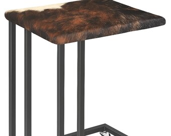 Può includere: Tavolino con piano quadrato con motivo a pelle di mucca marrone e bianco. Ha una struttura in metallo nero e quattro piccole ruote. Design moderno e funzionale, adatto a vari ambienti interni.