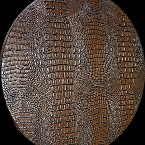 May include: A close-up of a brown faux leather round coaster with a crocodile skin pattern.