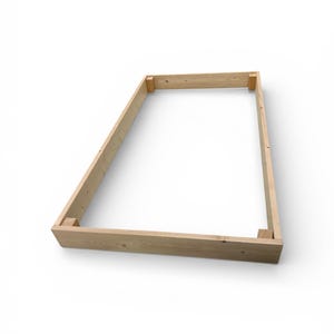 May include: A rectangular wooden frame, constructed from light-colored lumber, is presented against a white backdrop. The frame is assembled with corner joints, showcasing the natural wood grain and texture. The design suggests a potential for a raised garden bed or similar structure.