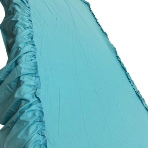 Pu&ograve; includere: Una balza per letto color turchese tinta unita con bordo arricciato lungo i lati. Il tessuto presenta una consistenza liscia e opaca con pieghe visibili su tutta la superficie, creando un aspetto morbido e stratificato sui bordi e sul fondo.