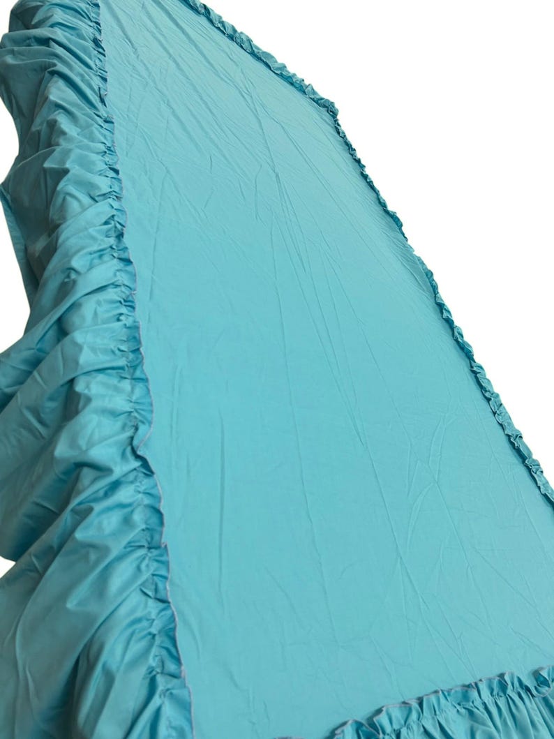 Pu&ograve; includere: Una balza per letto color turchese tinta unita con bordo arricciato lungo i lati. Il tessuto presenta una consistenza liscia e opaca con pieghe visibili su tutta la superficie, creando un aspetto morbido e stratificato sui bordi e sul fondo.